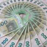 Close-up of a fan of 100 euro banknotes arranged in an artistic circle pattern on a textile surface.